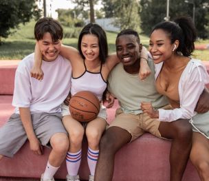 Happy multiracial friends embracing on bench after basketball training