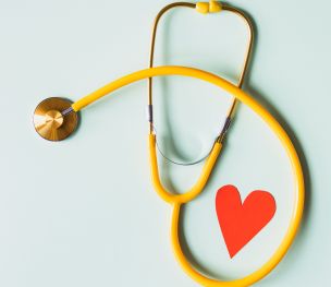 Medical stethoscope with red paper heart on white surface